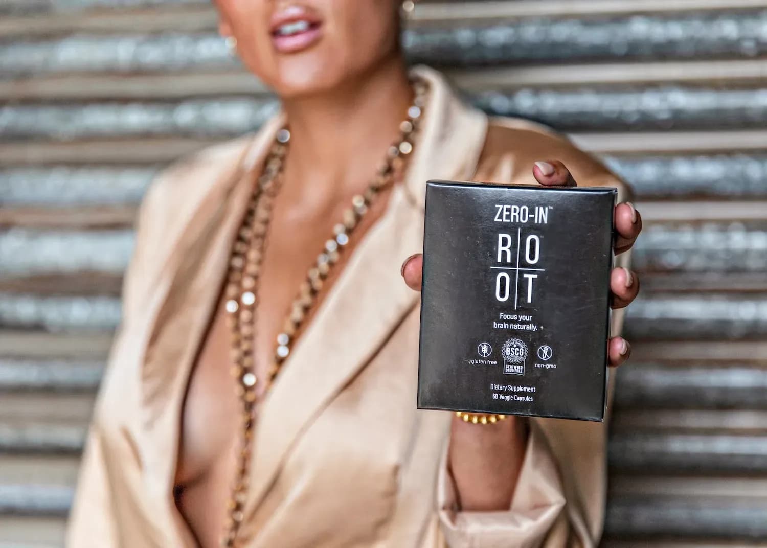 Blurred person in a beige blazer holding up a black ROOT ZERO-IN box in front of a metal shutter