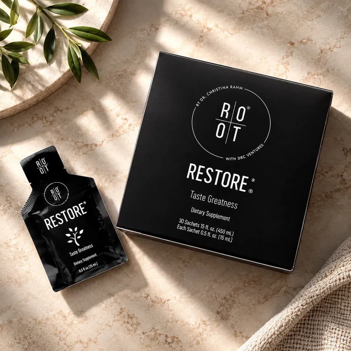 Uma saqueta preta Restore e uma caixa preta Restore sobre uma superfície de mármore, com um ramo de oliveira e uma toalha dobrada ao lado